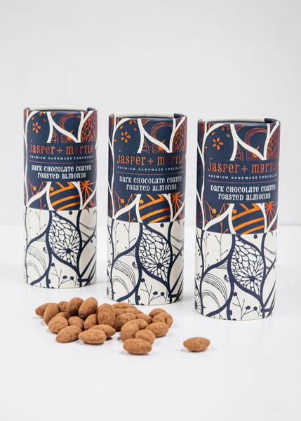 Three cylindrical packages of Jasper + Marty's dark chocolate covered roasted almonds on a white background.